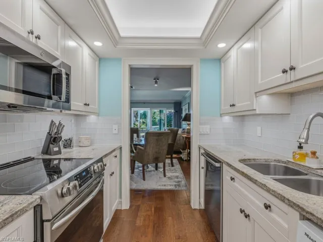 Kitchen featuring appliances with stainless steel finishes, dark wood-style floors, white cabinets, light stone counters, and recessed lighting