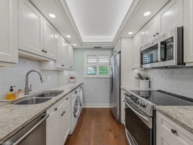 Kitchen with appliances with stainless steel finishes, light stone countertops, dark wood-type flooring, white cabinetry, and recessed lighting