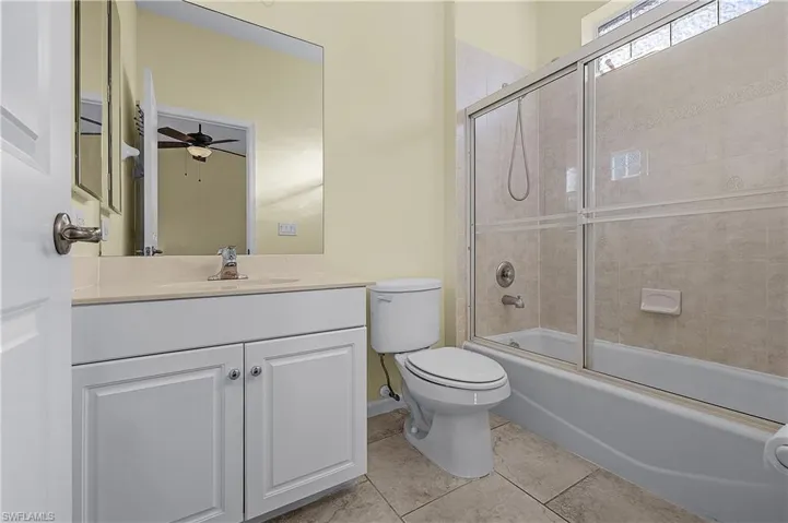 Full bathroom with combined bath / shower with glass door, vanity, ceiling fan, and light tile patterned floors