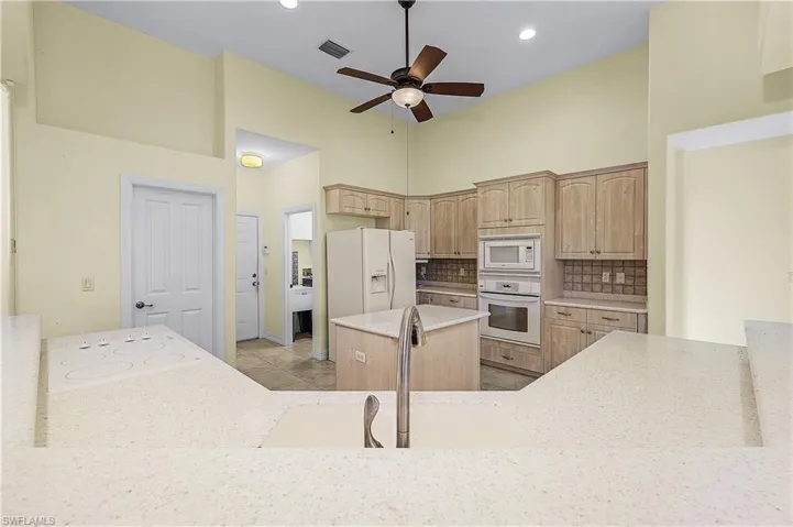 Kitchen with light brown cabinetry, white appliances, a center island, a high ceiling, and decorative backsplash