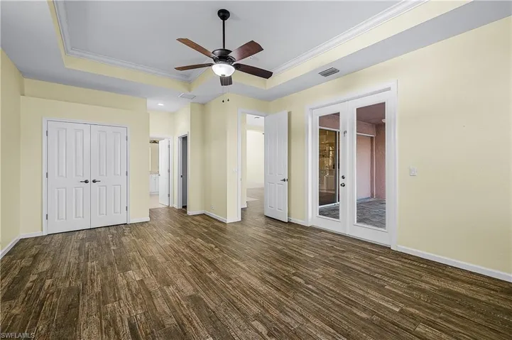 Unfurnished bedroom featuring crown molding, a tray ceiling, dark wood-type flooring, a ceiling fan, and french doors