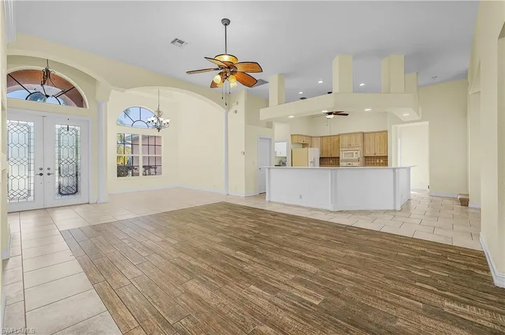 Unfurnished living room with ceiling fan, a high ceiling, french doors, a chandelier, and light tile patterned floors