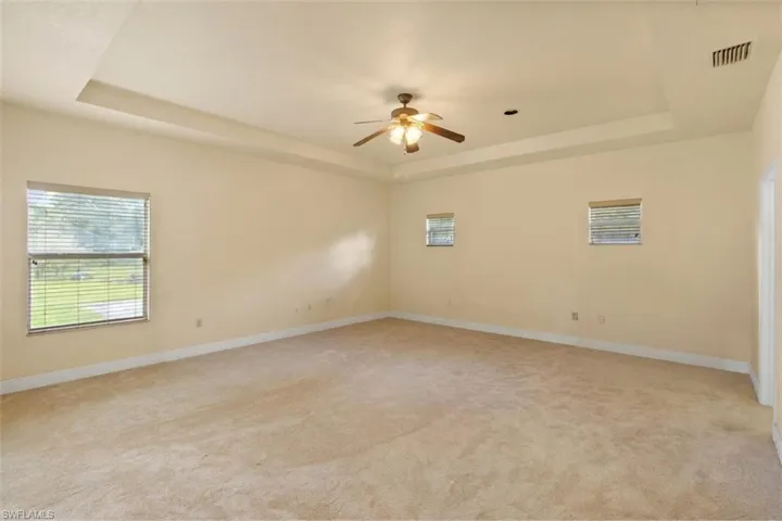 Expansive carpeted room featuring a tray ceiling, ceiling fan with integrated lighting, two windows with blinds, and recessed lighting
