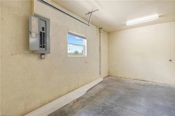 Utility space featuring concrete flooring, textured walls, a single window, and overhead fluorescent lighting