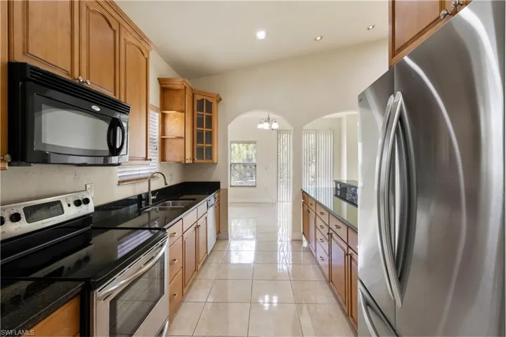 Kitchen featuring wood cabinetry, black countertops, stainless steel appliances, and tile flooring