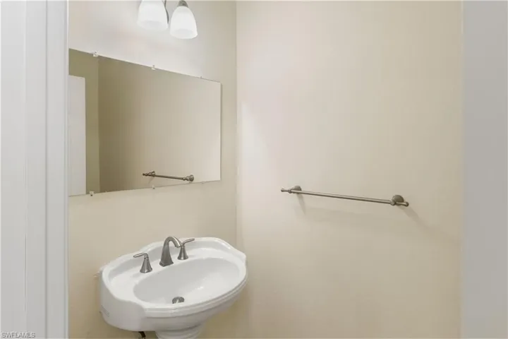 Pedestal sink with a two-handle faucet, illuminated by an overhead light fixture