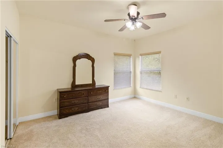 Bedroom featuring light beige carpeting, two windows with horizontal blinds, a ceiling fan with integrated lighting, and a closet with mirrored sliding doors