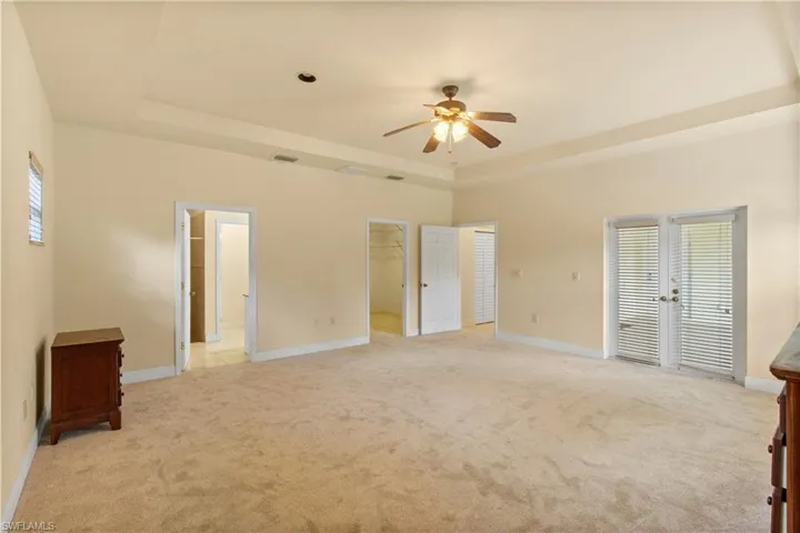 Spacious room featuring neutral carpeting, a tray ceiling with a ceiling fan, and double French doors with integrated blinds