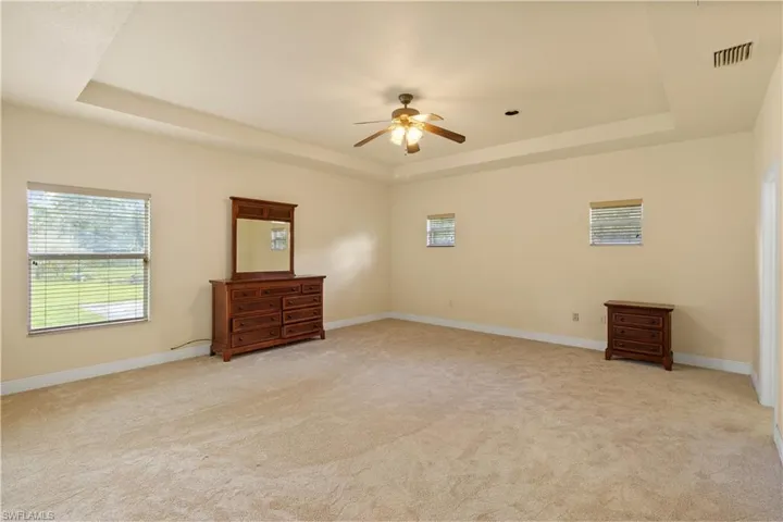 Spacious room featuring a tray ceiling with a ceiling fan, neutral carpeting, and multiple windows with blinds