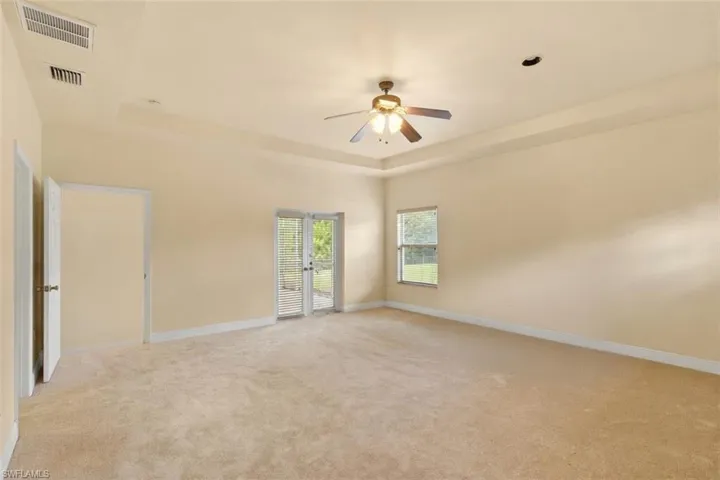 Spacious room featuring tray ceiling, ceiling fan, neutral carpet flooring, double French doors with blinds, and a single window