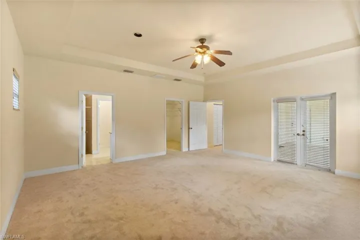 Spacious room featuring neutral carpeting and a tray ceiling with a built-in ceiling fan