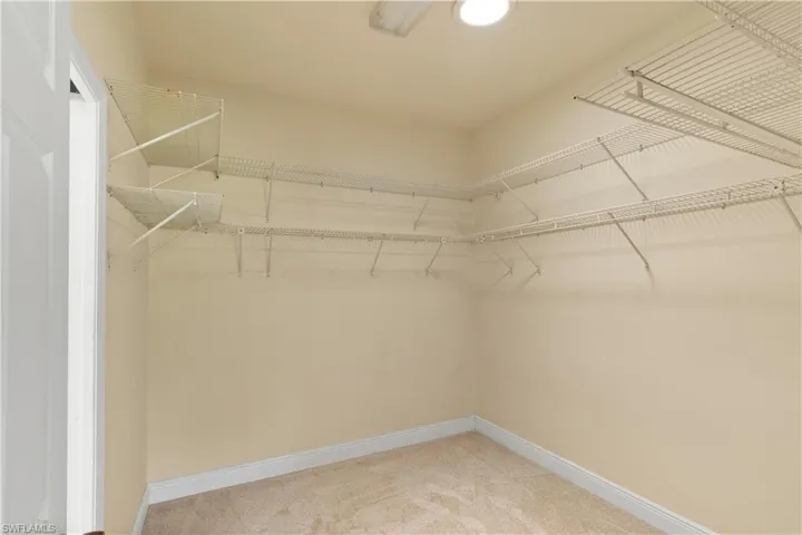 Walk-in closet featuring light beige walls, cream carpet flooring, white baseboards, and comprehensive wire shelving system