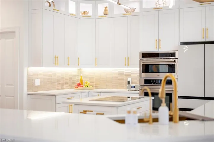 Kitchen with white cabinets, double oven, light stone counters, and freestanding refrigerator