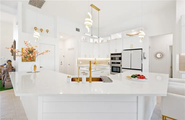 Kitchen with white cabinetry, backsplash, freestanding refrigerator, light stone counters, and hanging light fixtures