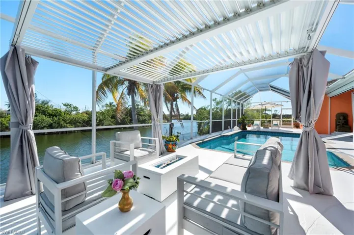 Outdoor pool featuring a sunroom, a patio, a water view, a lanai, and an outdoor living space with a fire pit