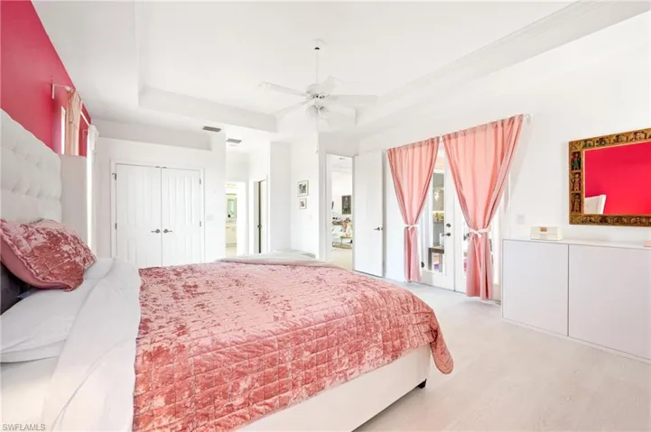 Bedroom featuring light wood finished floors, ceiling fan, a tray ceiling, ornamental molding, and two closets
