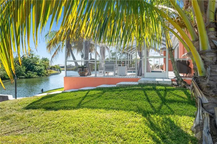 View of green lawn with a sunroom, a water view, and glass enclosure
