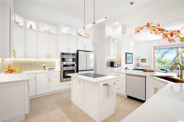 Kitchen with tasteful backsplash, white cabinets, glass insert cabinets, hanging light fixtures, and white appliances