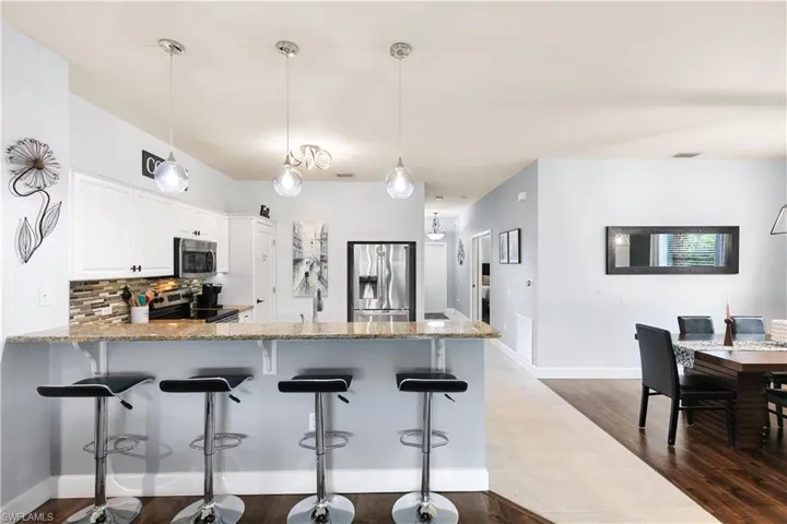 Kitchen featuring white cabinetry, tasteful backsplash, appliances with stainless steel finishes, a peninsula, and dark wood finished floors