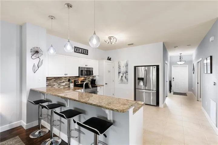 Kitchen with light stone counters, tasteful backsplash, a breakfast bar, a peninsula, and stainless steel appliances