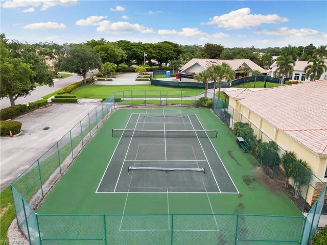 View of tennis court with a yard and fence