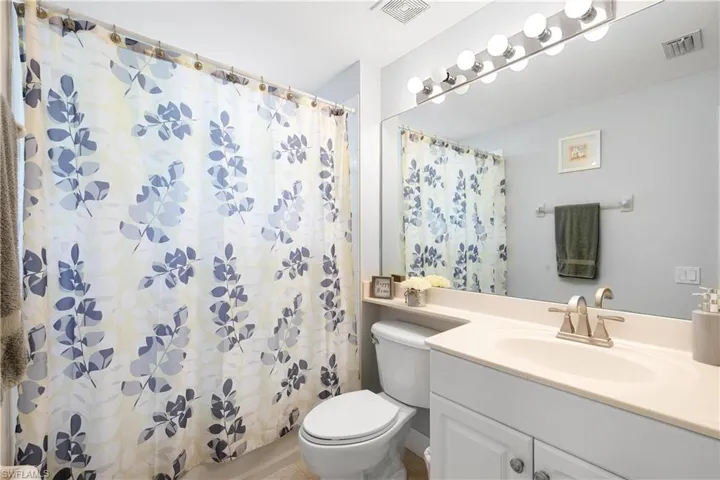 Full bath with curtained shower, visible vents, toilet, and vanity