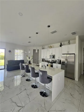 Kitchen with appliances with stainless steel finishes, a kitchen bar, light countertops, and white cabinets