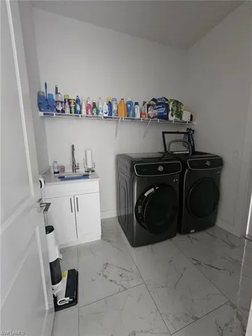 Washroom featuring washer and dryer, cabinet space, light marble finish flooring, and baseboards