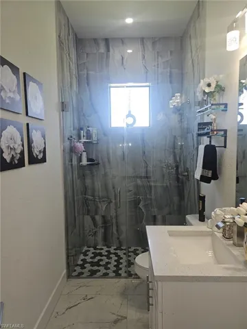 Full bath featuring marble finish floors, toilet, a marble finish shower, baseboards, and vanity