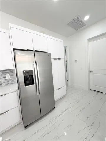 Kitchen with white cabinets, stainless steel fridge with ice dispenser, light marble finish floors, modern cabinets, and recessed lighting