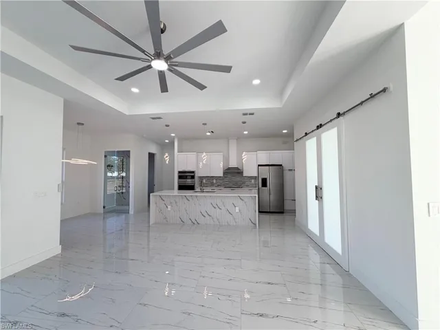 Kitchen with a raised ceiling, stainless steel appliances, a ceiling fan, white cabinetry, and a spacious island
