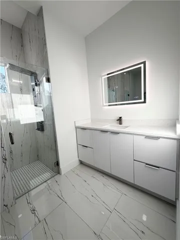 Bathroom with vanity, a marble finish shower, and light marble finish floors