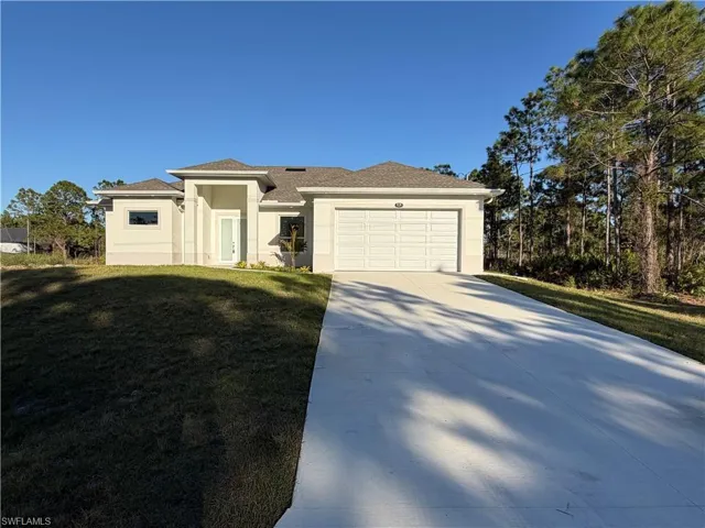 Prairie-style house with a front lawn, driveway, an attached garage, stucco siding, and a shingled roof
