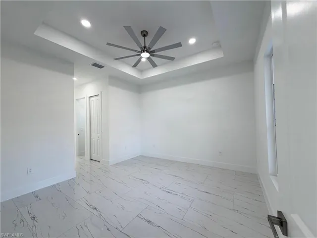 Empty room with light marble finish flooring, ceiling fan, recessed lighting, and a raised ceiling