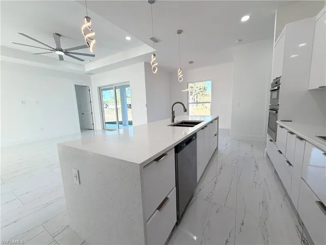 Kitchen with modern cabinets, hanging light fixtures, light marble finish flooring, plenty of natural light, and two tone cabinets