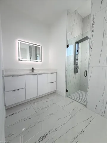 Bathroom featuring a marble finish shower, vanity, and light marble finish floors