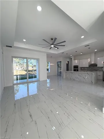 Unfurnished living room featuring a raised ceiling, plenty of natural light, recessed lighting, and ceiling fan