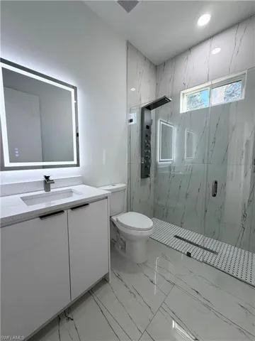 Bathroom with vanity, a marble finish shower, and light marble finish flooring