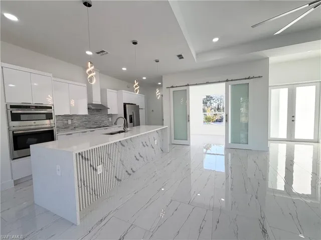 Kitchen featuring pendant lighting, white cabinets, stainless steel appliances, and light stone countertops