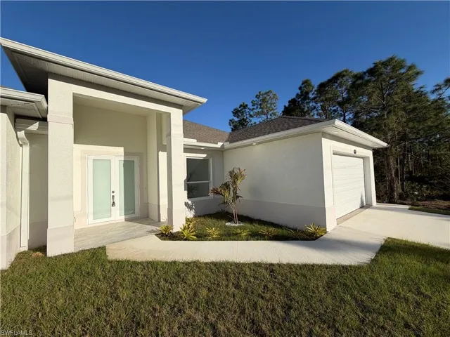 Entrance to property with a garage, stucco siding, french doors, driveway, and a yard