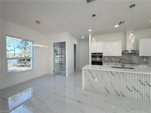 Kitchen with pendant lighting, light stone counters, white cabinetry, decorative backsplash, and modern cabinets