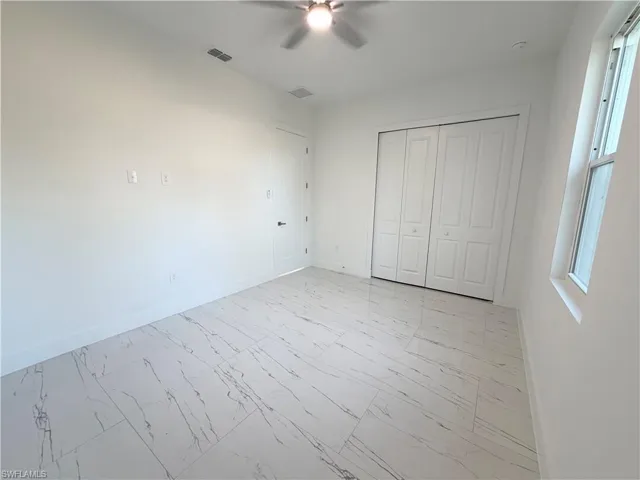 Unfurnished bedroom featuring light marble finish flooring, a closet, and ceiling fan