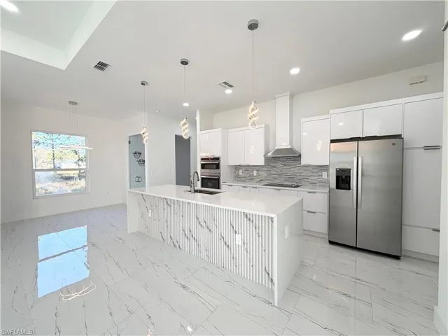 Kitchen with stainless steel appliances, light marble finish flooring, hanging light fixtures, backsplash, and white cabinetry