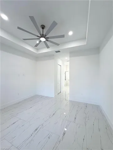 Unfurnished room with a raised ceiling, recessed lighting, ceiling fan, and light marble finish floors