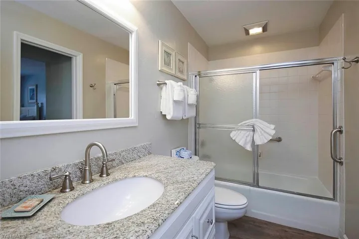 Full bath with bath / shower combo with glass door, wood finished floors, vanity, and toilet