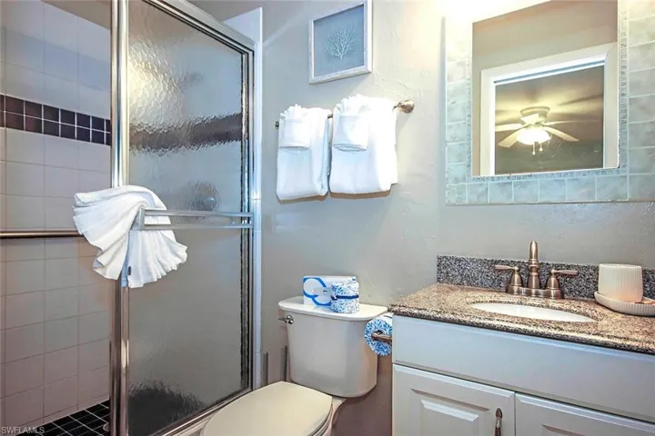 Full bath featuring vanity, a shower stall, toilet, and a ceiling fan