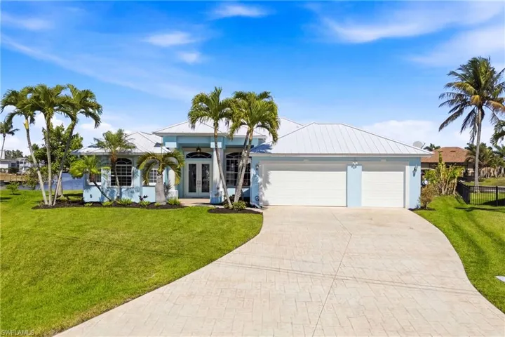 Front of home highlighting wide driveway, tropical greenery, and an inviting entryway.