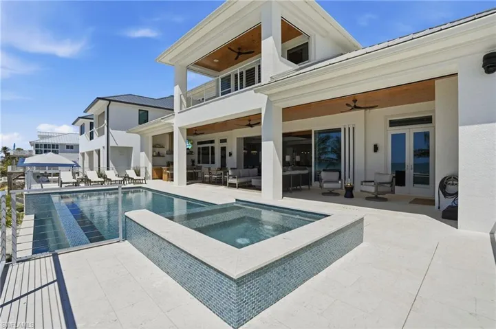 Rear view of house featuring a balcony, a ceiling fan, an outdoor hangout area, a patio area, and a pool with connected hot tub - Virtually Edited Image