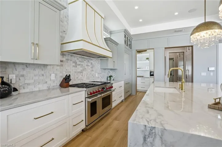 Kitchen with light stone countertops, range with two ovens, light wood-style flooring, decorative backsplash, and white cabinetry - Virtually Edited Image