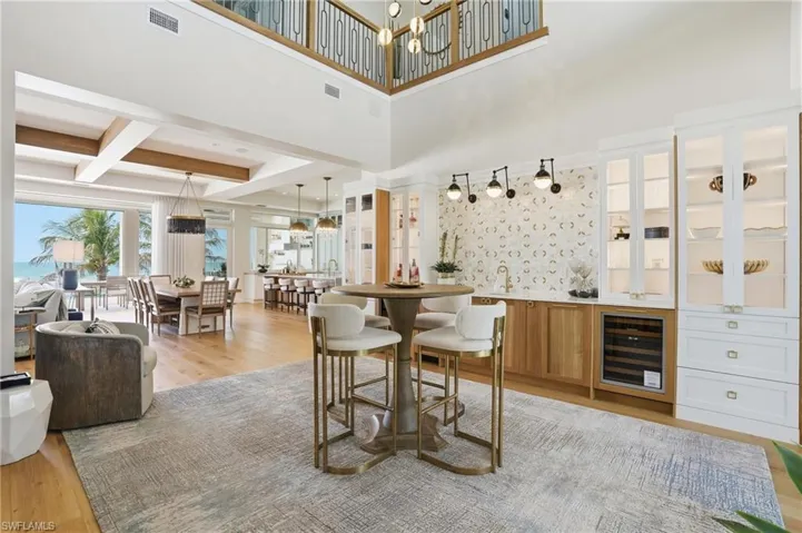 Dining room featuring light wood-style floors, wine cooler, a chandelier, a high ceiling, and wet bar - Virtually Edited Image